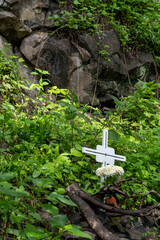 cross on the sidewalk of a deceased person huentitan canyon in guadalajara, mountains and trees, green vegetation and sky with clouds, mexico