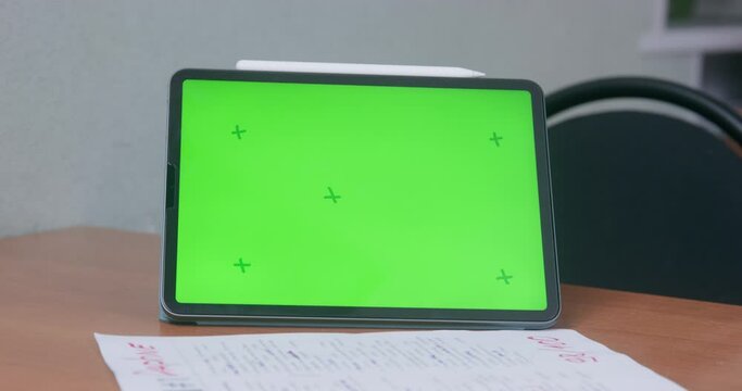 Documents, digital pencil and tablet in case are on table, green chromakey with guide marks on display, front view. Gadget for work, online education or creativity. Template for advertising.