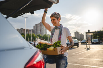 One woman mature caucasian female standing by the back trunk of her car on the parking lot of the supermarket shopping mall or grocery store with vegetables food in box putting them in the vehicle © Miljan Živković
