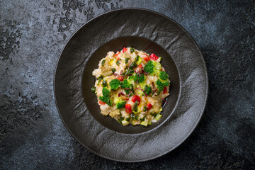 vegetable risotto with fresh vegetables and broccoli on dark plate on dark stone table top view