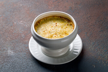 French onion soup with cheese on top on dark stone table