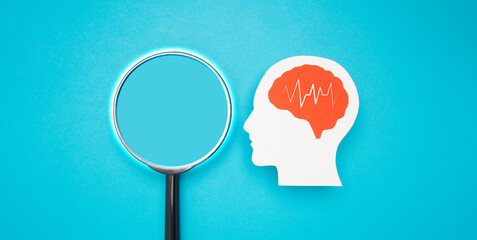 A brain shape made from paper and a magnifying glass on a light blue background