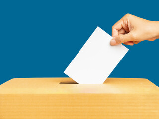 Obraz premium Hand voter holding ballot paper putting into the voting box at place election against a blue background
