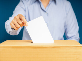 Hand voter holding ballot paper putting into the voting box at place election against a blue background