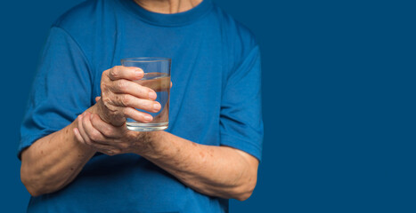 Close-up of hands senior woman trying to hold a glass of water