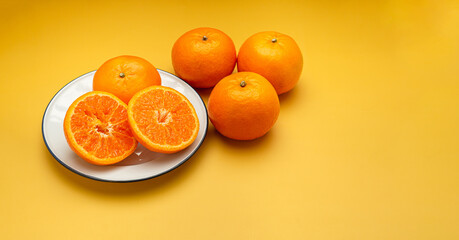 Pile of fresh oranges and half fruit on a white plate and yellow background