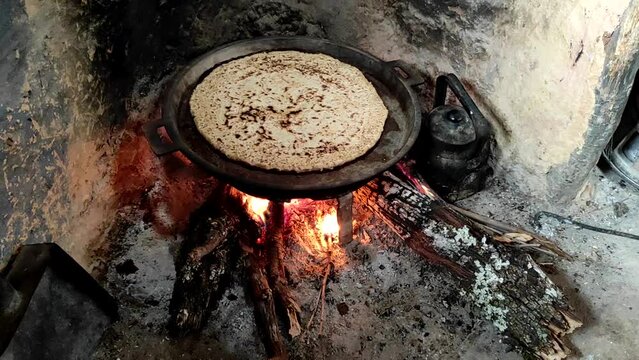 Close-up of Cooking bread in a cast iron skillet resting on trivets, over an oak wood fire in a large stone fireplace in a traditional kitchen. Medieval kitchen utensils. Morocco.