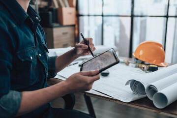 Engineering working with drawings inspection on tablet in the office and Calculator, triangle ruler, safety glasses, compass on Blueprint. Engineer, Architect, Industry and factory concept.