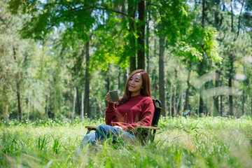 Portrait image of a beautiful young asian woman drinking coffee while sitting on a chair in the park