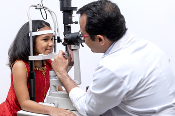 Indian girl and optometrist doing eye test with slit lamp in modern ophthalmology clinic, checking retina of a girl eye - obrazy, fototapety, plakaty