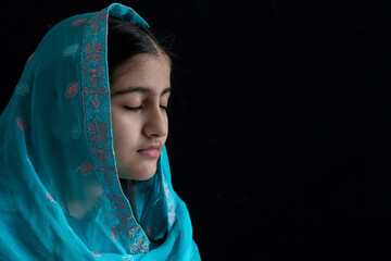Little Muslim girl wearing blue hijab and close her eyes, black background, side view