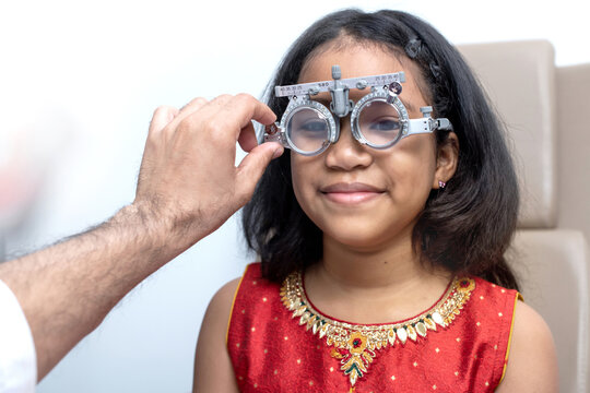 Optometrist uses an trial frame to examine the vision of a little Indian child girl at an ophthalmology clinic, Vision devices for checking vision