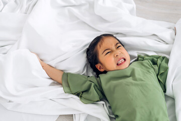 Portrait of happy smiling little child asian girl having fun lying in white bed and looking at camera at home.