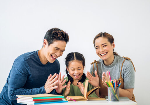 Portrait enjoy happy love asian family father and mother with little asian girl learn and study on table.Mom and dad with young girl writing with book make homework in homeschool at home.Education