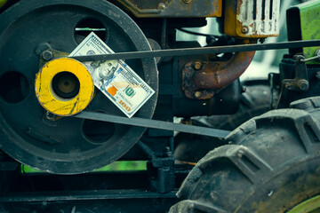 A hundred dollar bill lies on the engine of a small rural walk-behind tractor for tillage