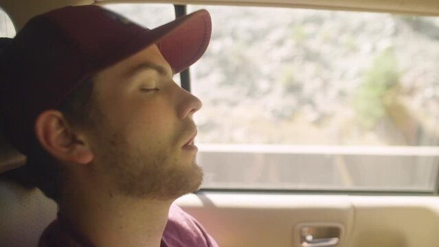 Attractive young tired white man gen Z millennial falls asleep in the back of car with mouth open during a road trip van life adventure in slow motion