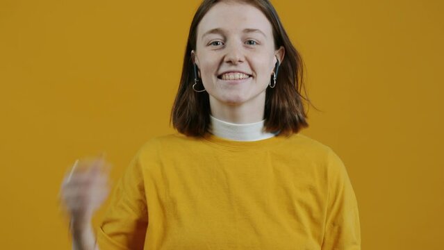 Portrait of modern girl using earpods and nodding head dancing on yellow background. Devices and contemporary technologies concept.
