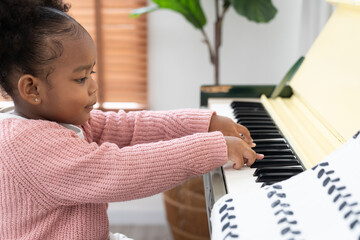 Little girl playing piano at home. African American kid practice learning piano at nursery school....