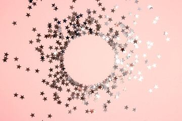 Round frame from silver star shaped glitter confetti on pink background.