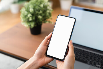 Hands holding smartphone with mockup of blank screen on sofa in living room.