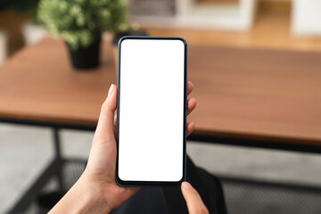 Hands holding smartphone with mockup of blank screen on sofa in living room.