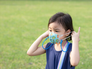 Dramatic portrait of 4 years old cute baby Asian girl, little preschooler child with adorable short hair  with worried expression takes off protective face mask standing outdoor