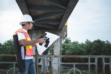Asian male engineer standing on the bridge and looking at blueprint for planning to improve the...