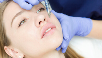 A woman with beautiful clear skin. A cosmetologist makes injections to increase the lips and...