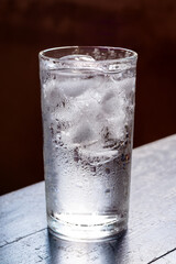 Glass of water with ice on wooden dark natural light background.