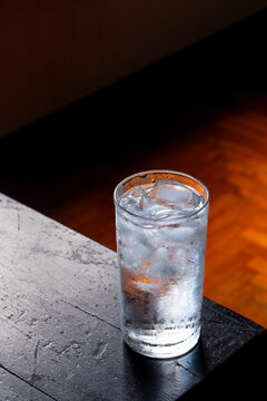 Glass of water with ice on wooden dark natural light background.