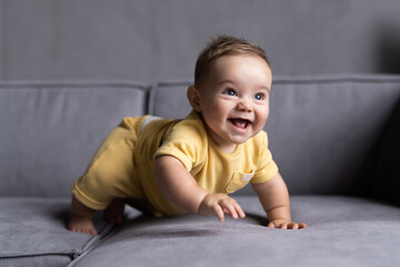 Portrait of lovely baby boy with blue eyes and blue shirt sitting on couch and looking up, blurred toys in background.