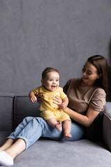 Mother and baby laugh together at home. They are sitting on the sofe in a brightly lit living room...