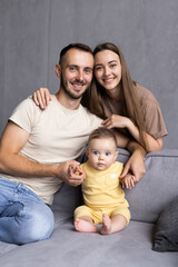 Fototapeta premium Cheerful family are spending funny time while sitting on sofa in bright room. Happy parenthood concept