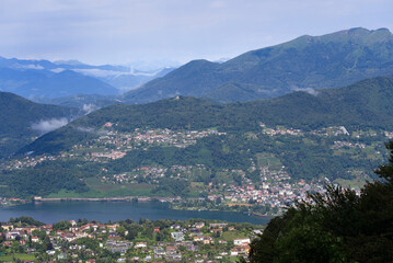 Fototapeta na wymiar Scenic landscape with mountain panorama and Lake Lugano seen from local mountain San Salvatore at City of Lugano on a cloudy summer day. Photo taken July 4th, 2022, Lugano, Switzerland.