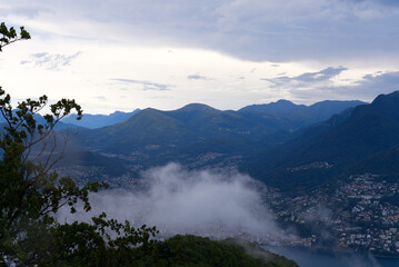 Scenic landscape with mountain panorama and Lake Lugano seen from local mountain San Salvatore at City of Lugano on a cloudy summer day. Photo taken July 4th, 2022, Lugano, Switzerland.