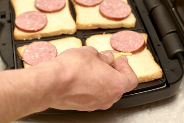 a man cooking sandwiches in a sandwich maker lays out pieces of cheese on bread