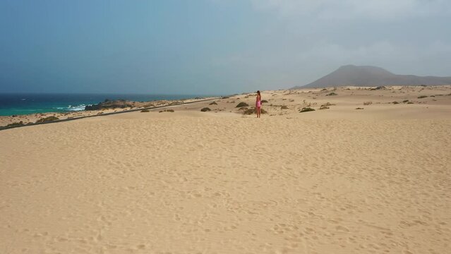 Eoung woman enjoys relaxing. Sand dunes on the seashore. Summer vacations, wild desert nature in Corralejo. Coast of the Atlantic Ocean, blue water. Feel freedom. Fuerteventura. Canary Islands, Spain