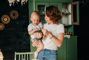 Loving happy mom with baby daughter on her hands, funny child girl infant while mother is cooking...