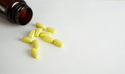 Vitamins for women. Yellow capsules on a white background with a brown bottle.               