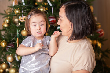 cute baby with down syndrome with mom near the christmas tree, happy new year and Christmas