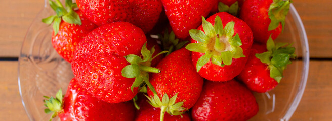 Many red strawberries on glass plate and wooden table top view banner
