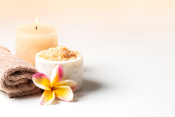 SPA composition , burning candle, towel, salt scrub and frangipani flower on beige background>relax and massage treatment