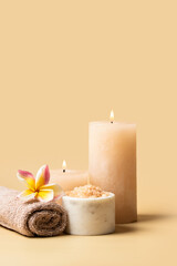 SPA still life composition , burning candle, towel, salt scrub and frangipani flower on beige background . Relax and massage treatment