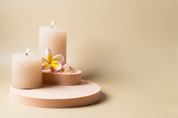 SPA concept , burning candle, towel, salt scrub and frangipani flower on podiums beige background. Beauty tretmets and massage concept