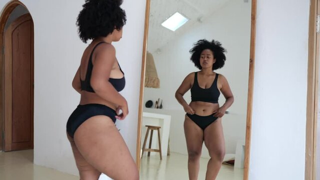 African Asian woman in black lingerie examines her cellulite in front of a mirror, and cannot believe that her body has become so fat. Obese women from eating fast food around the world.