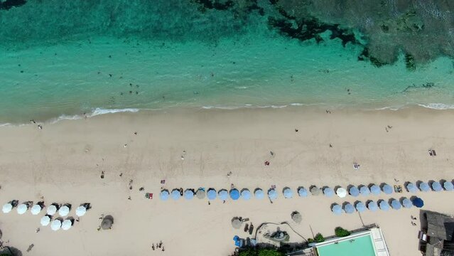 Aerial image of MELASTI BEACH in ULUWATU BALI, with several hotels and sunshades visible, as well as waves coming near the beach and people strolling in the sand was captured by Drone
