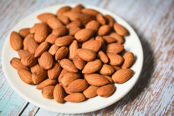 Almonds nuts on white palte, Delicious sweet almonds on the wooden table background, roasted almond nut for healthy food and snack