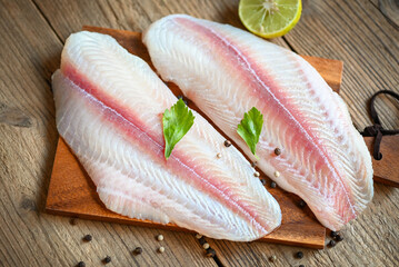 fish fillet on wooden board with ingredients for cooking, fresh raw pangasius fish fillet with herb...