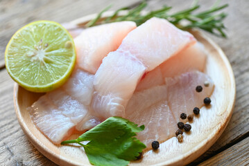 fish fillet on wooden plate with ingredients for cooking, fresh raw pangasius fish fillet with herb...