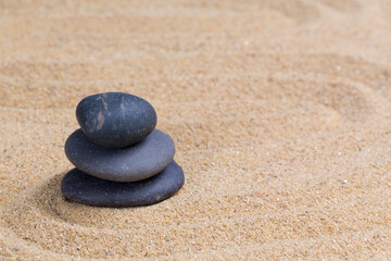 Fototapeta na wymiar Black spa stone on the sea sand with copy space. Concept for harmony spirituality and spirituality. zen stones and buddhism Balance relaxation meditation for life.